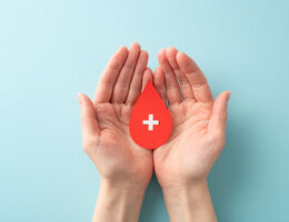 Cupped hands hold a red paper heart with a white cross symbol on it.