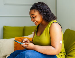 A woman with a continuous glucose monitor on her arm checks her numbers on her smartphone.