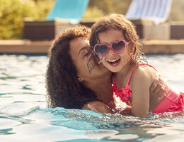 A smiling woman holds a smiling child in a swimming pool.