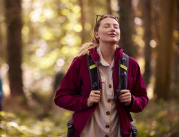 A hiker in a sunlit forest stands for a moment with her eyes closed.