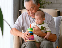 An older man holds a stacking toy for the baby on his lap.