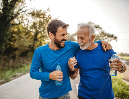 A man and his father carrying water bottles laugh together after a workout.
