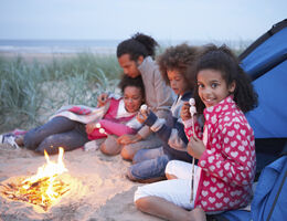 A family of four make s'mores by a campfire on a beach.