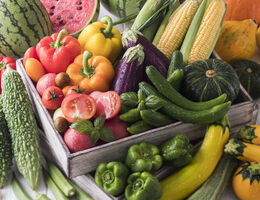 Summer fruits and vegetables fill and surround a crate.