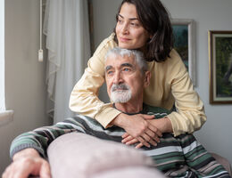 A woman bends to hug a seated older man.