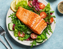 A slice of grilled salmon atop a plate of salad.